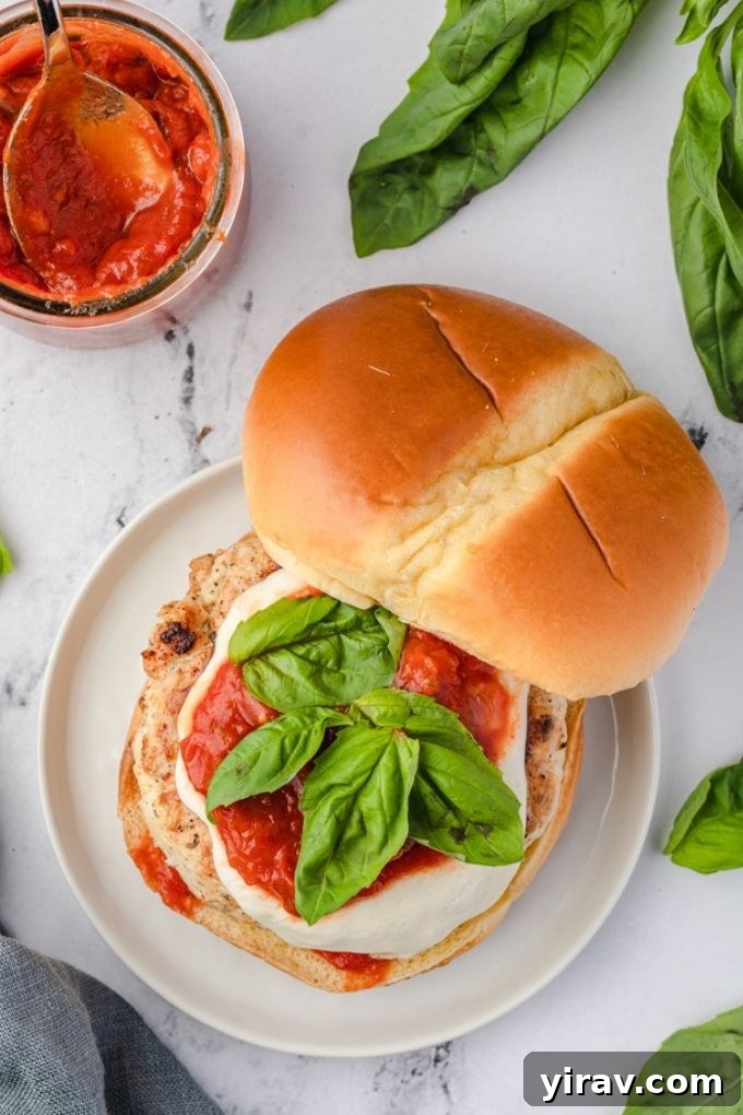 Inside view of a ground chicken parmesan burger with the top bun removed, showing layers of chicken patty, marinara, mozzarella, and basil