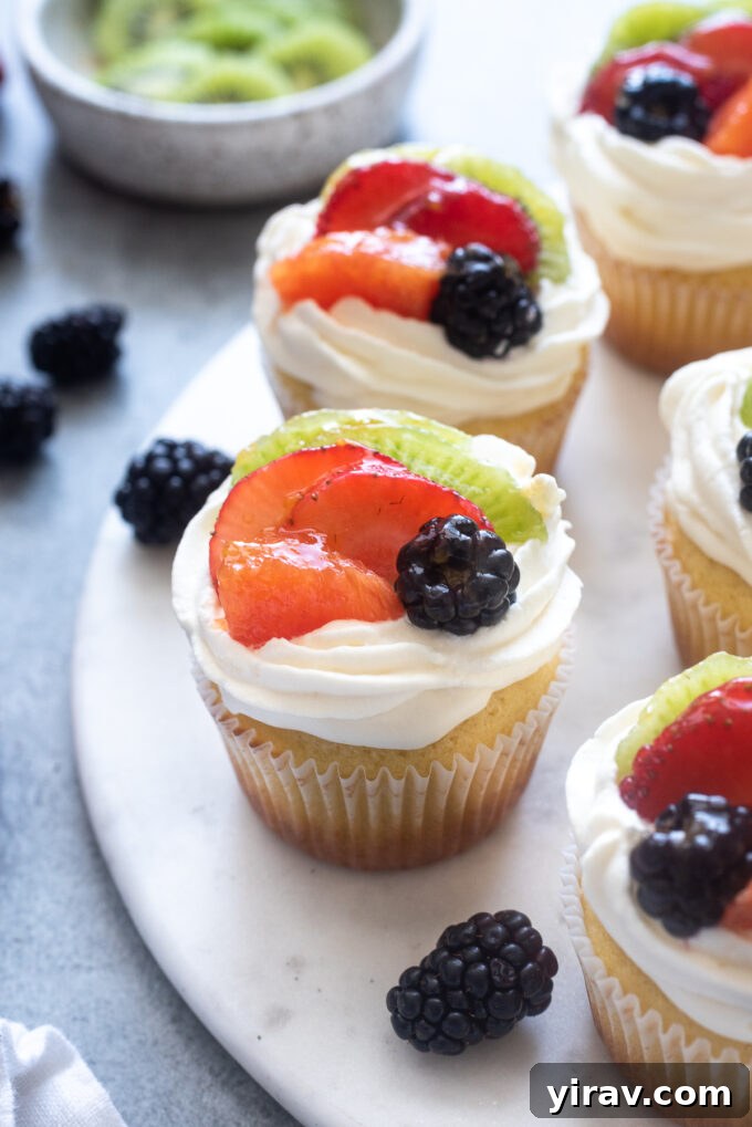 Fruit tart vanilla cupcakes on a serving board, showcasing vibrant fresh fruit and creamy frosting.