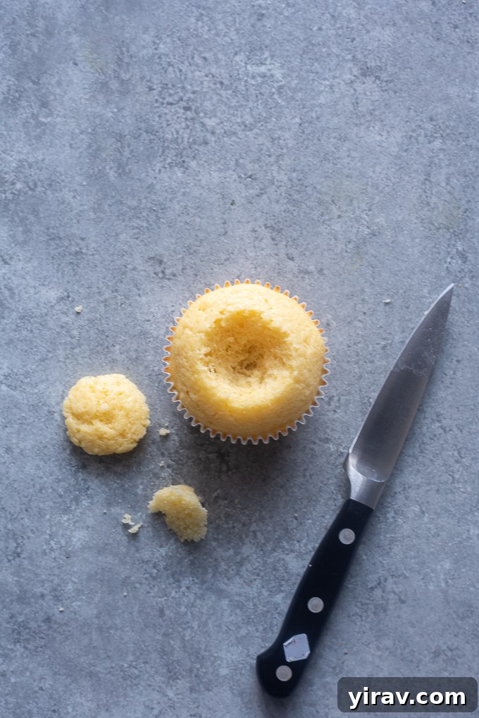 Vanilla cupcake with its center carefully cut out and a small cake plug removed, ready for filling.