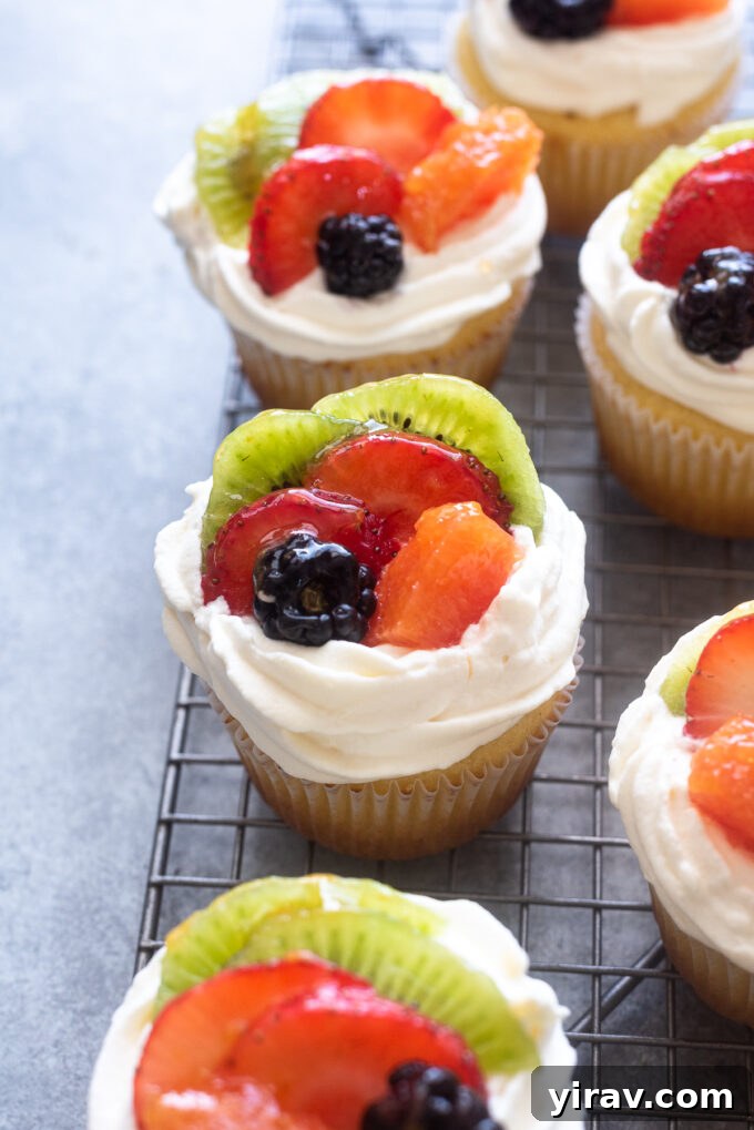Close-up of vanilla cupcakes with a decorative arrangement of fresh fruit on top, showcasing berries, kiwi, and orange segments.