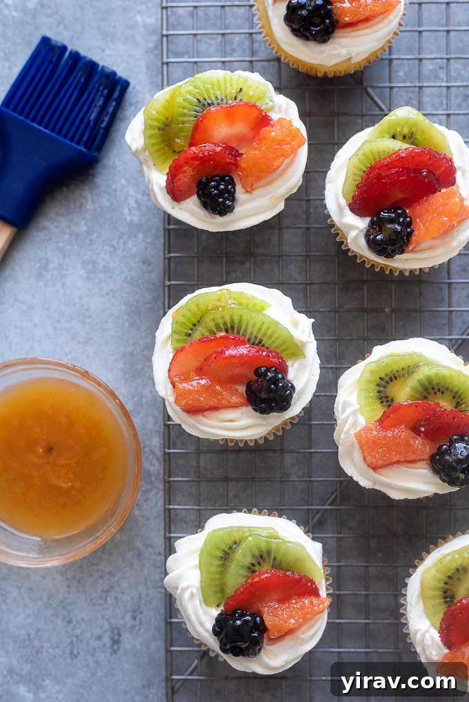 Decorated vanilla cupcakes with an artful arrangement of fresh fruit and a glossy jam glaze.