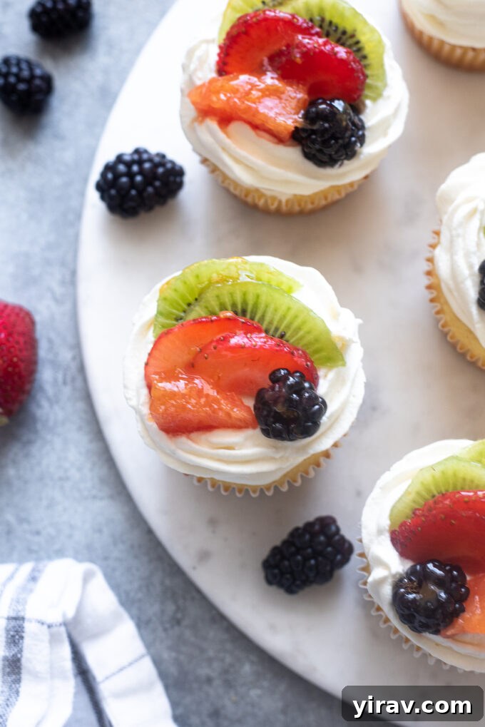 Vanilla cupcakes topped with whipped cream and fresh fruit, beautifully arranged for presentation.