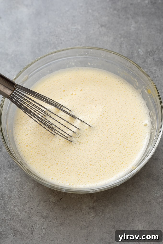 Hot milk mixture being slowly added to egg yolk mixture, demonstrating the tempering process.