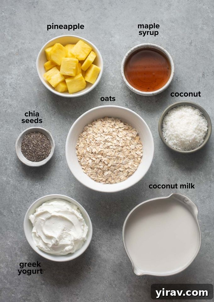 Pina colada overnight oats recipe ingredients laid out, including oats, chia seeds, shredded coconut, coconut milk, Greek yogurt, maple syrup, and fresh pineapple.