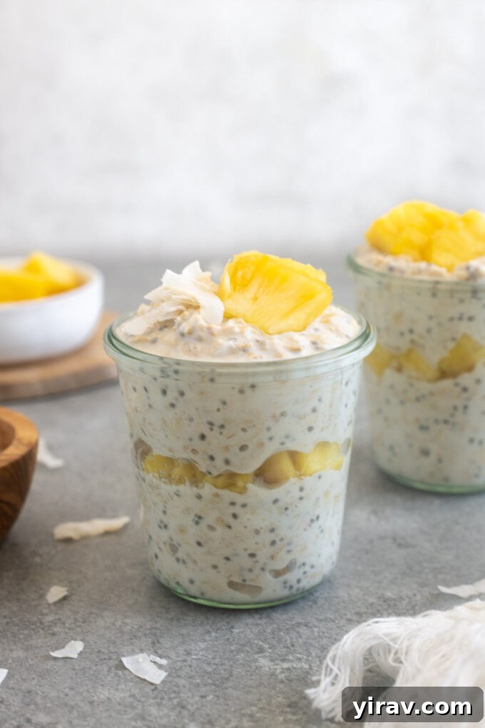 A jar of Pina Colada Overnight Oats topped with fresh pineapple, coconut flakes, and a spoon, ready to be eaten.
