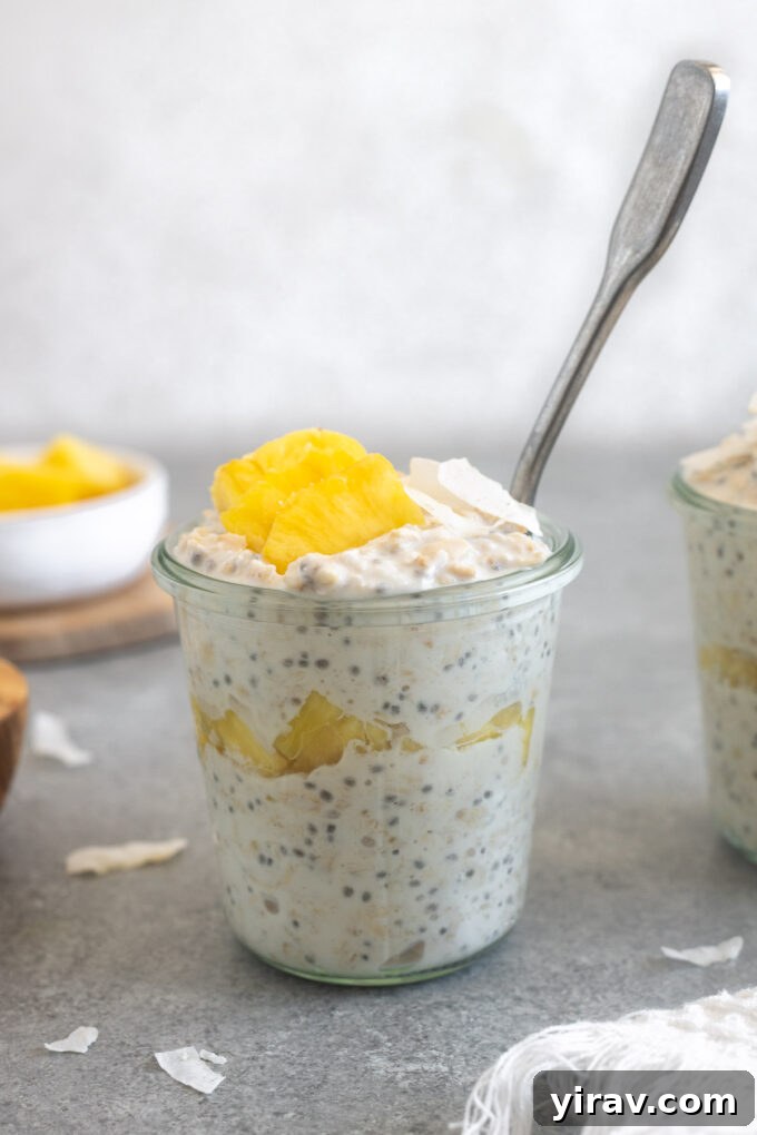 A jar of Pina Colada Overnight Oats with a spoon, showing the creamy texture and pineapple chunks.