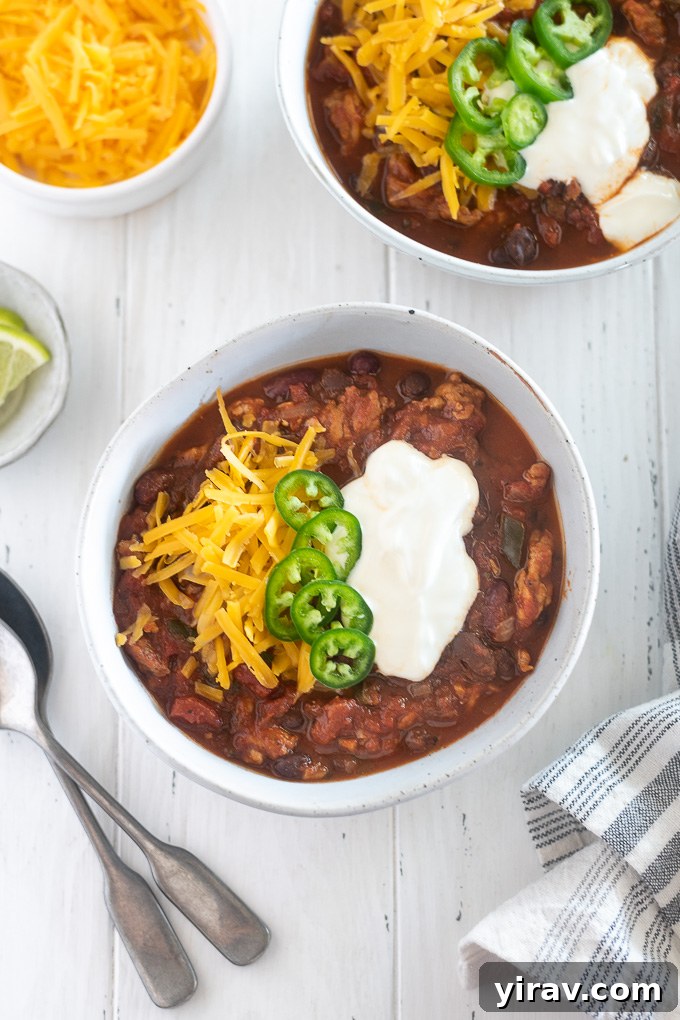 Close-up shot of a bowl of rich Slow Cooker Turkey Chili, generously topped with shredded cheddar cheese, a dollop of sour cream, and vibrant sliced jalapeños.