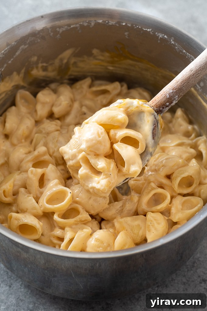 A spoonful of incredibly creamy mac and cheese being lifted over the pot, showcasing its smooth texture.