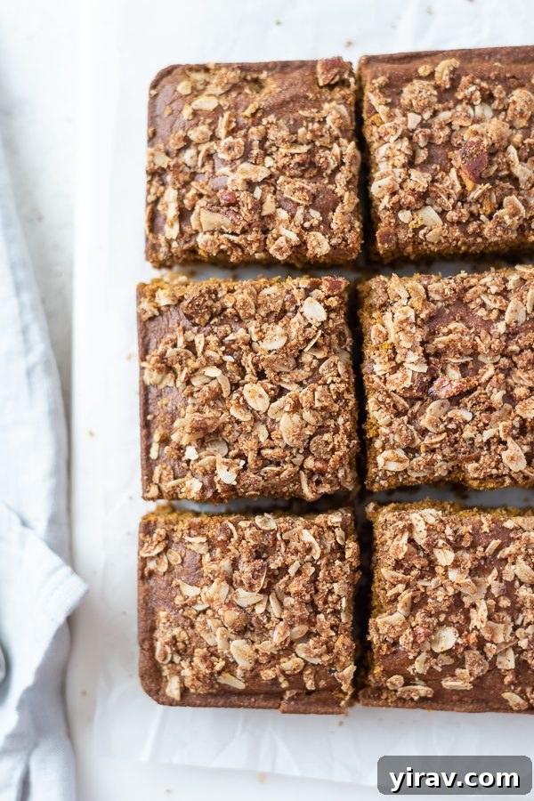 An inviting overhead shot of a freshly baked pumpkin coffee cake, expertly sliced into neat squares, revealing its rich, pumpkin-colored crumb and abundant oat pecan streusel.