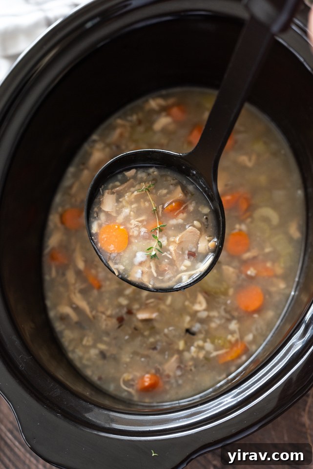 A ladle serving a generous portion of Slow Cooker Turkey Wild Rice Soup into a bowl.