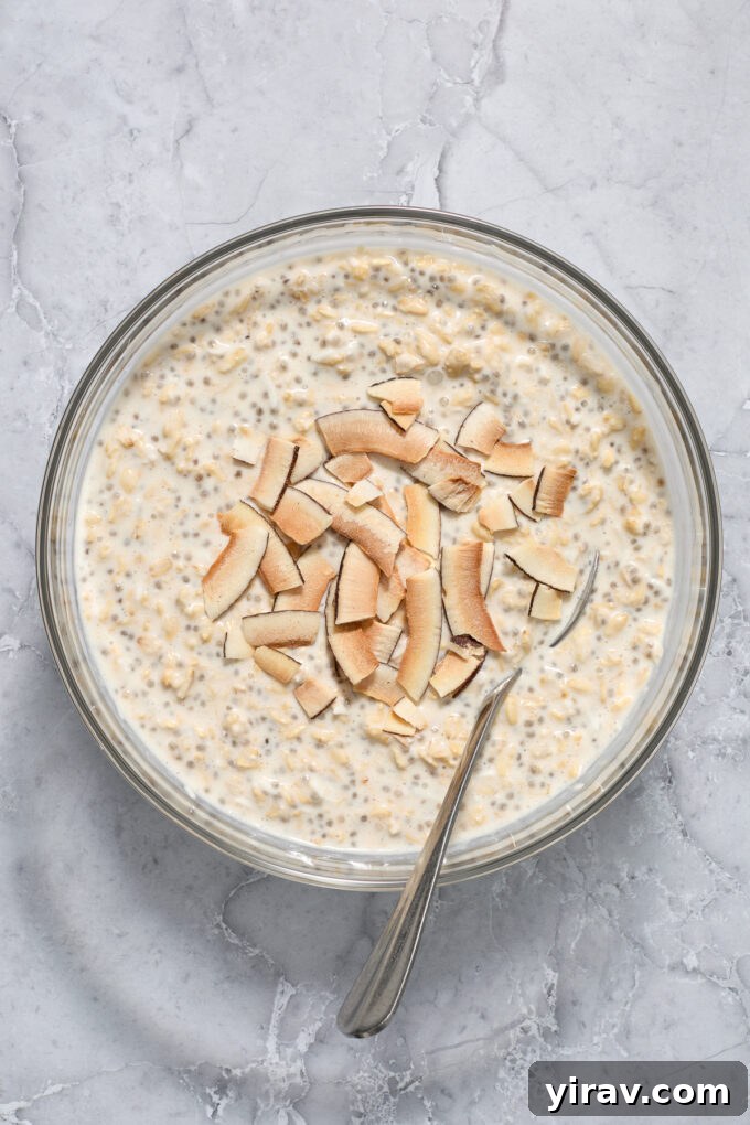 Coconut cream pie overnight oats in a mixing bowl, ready to be portioned, with a sprinkle of coconut flakes.