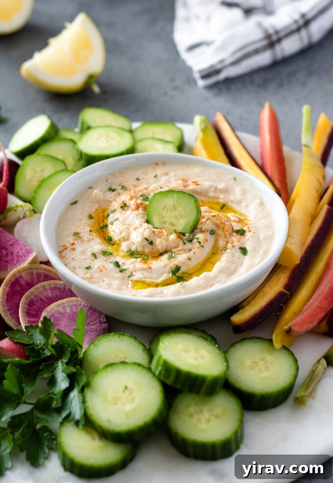 Creamy White Bean Hummus 2 A bowl of creamy white bean hummus garnished with a drizzle of olive oil and fresh herbs, surrounded by colorful vegetable sticks for dipping.