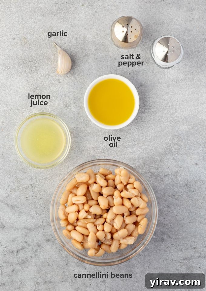 Creamy White Bean Hummus 4 Fresh ingredients for white bean hummus laid out on a kitchen counter: canned white beans, a bottle of olive oil, fresh garlic cloves, and bright yellow lemons.