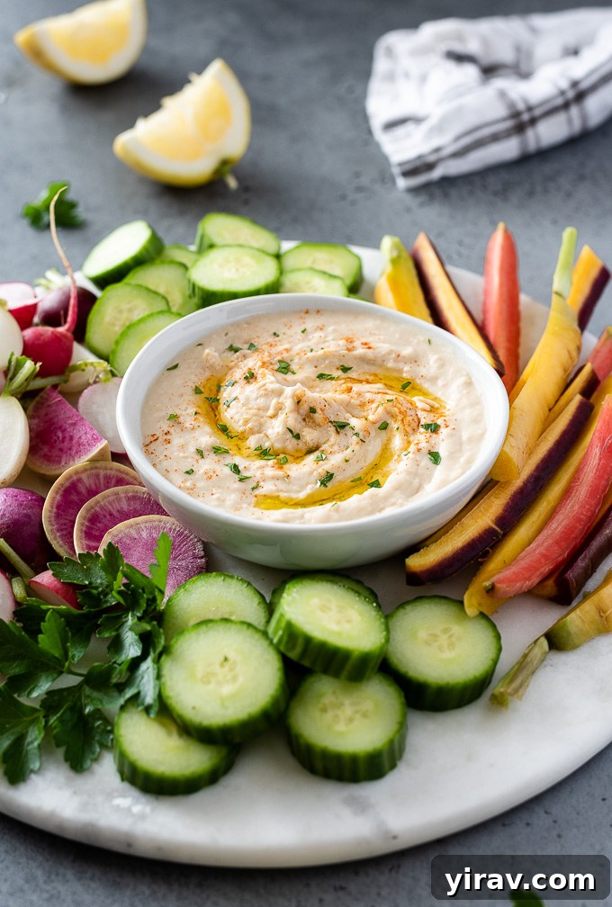 Creamy White Bean Hummus 6 A vibrant platter featuring a generous portion of white bean hummus, surrounded by an assortment of fresh, colorful vegetables like cucumber, bell peppers, carrots, and cherry tomatoes, ready for dipping.