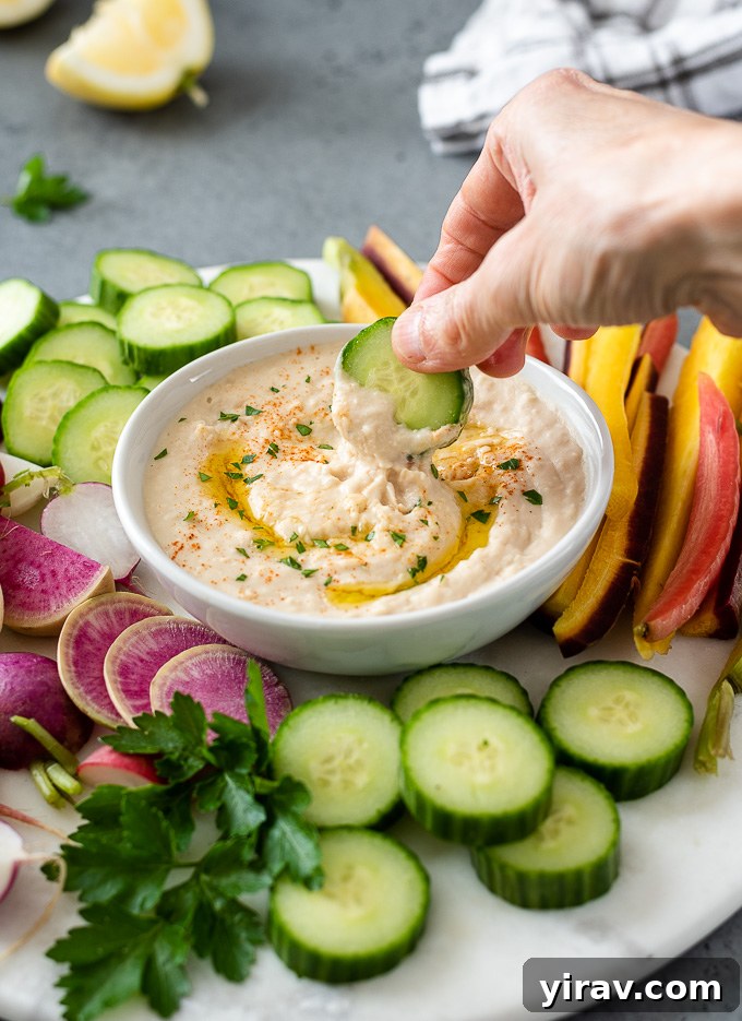 Creamy White Bean Hummus 7 A close-up shot of creamy white bean hummus in a rustic bowl, with a slice of cucumber being dipped into its smooth texture, highlighting its appealing consistency.