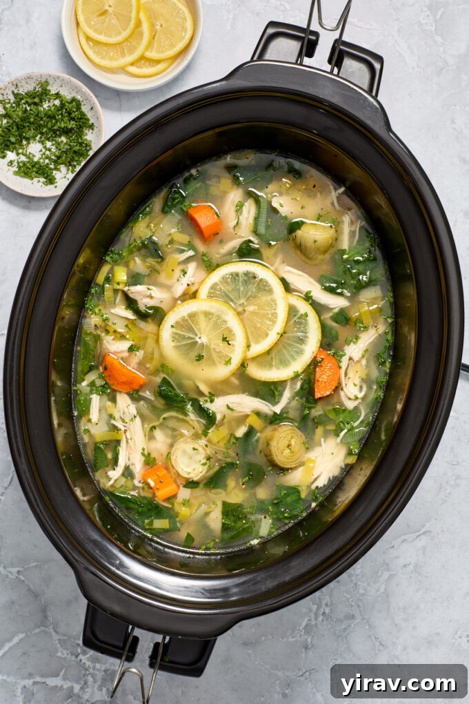 Lemon chicken artichoke soup in the slow cooker with lemon slices.