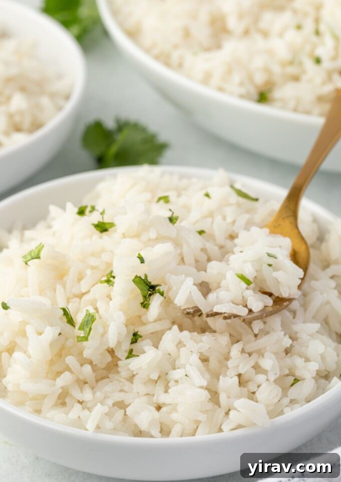 A bowl of creamy, fluffy coconut rice with a fork digging into it, garnished with fresh herbs