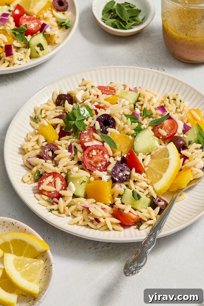 Orzo Greek salad on a serving plate with a fork.