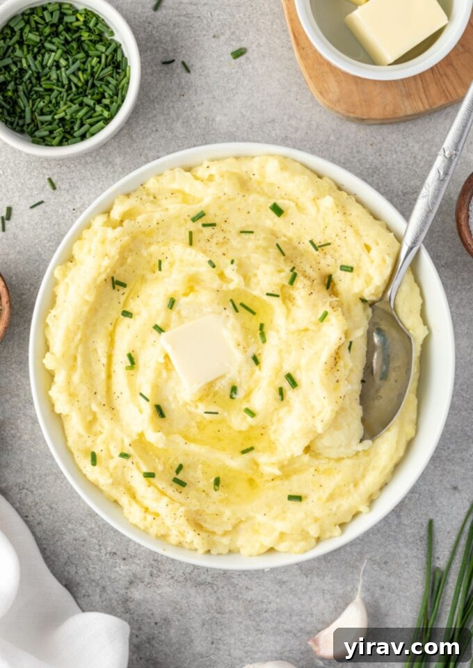 Sumptuous Yukon Gold Mashed Potatoes 2 A bowl of creamy Yukon Gold mashed potatoes with a serving spoon, garnished with fresh herbs and a pat of melting butter.
