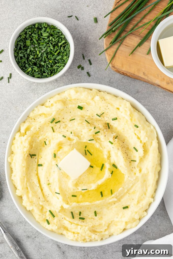Sumptuous Yukon Gold Mashed Potatoes 6 A close-up of a bowl of creamy Yukon Gold mashed potatoes, with butter melting on top and scattered fresh chives, ready to be served.