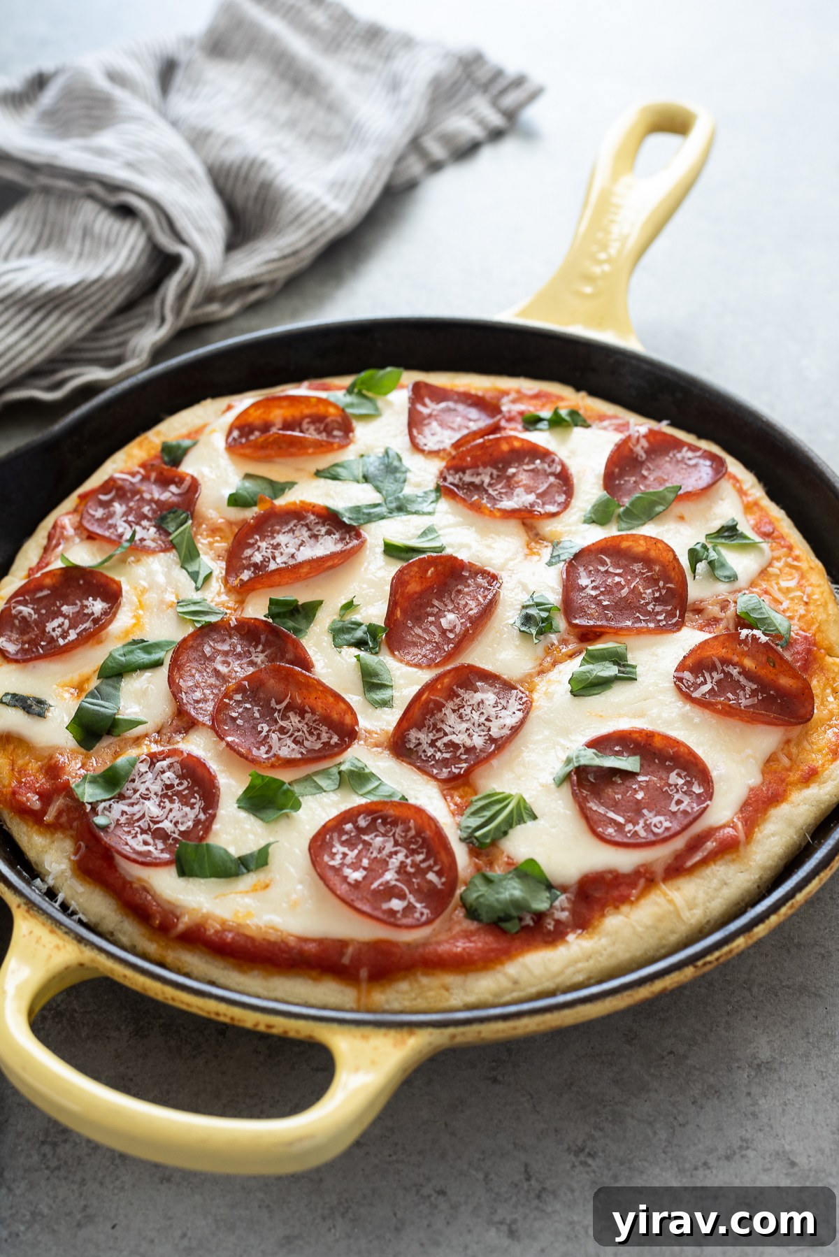 Homemade focaccia pizza with pepperoni and basil, sliced in a cast iron skillet.