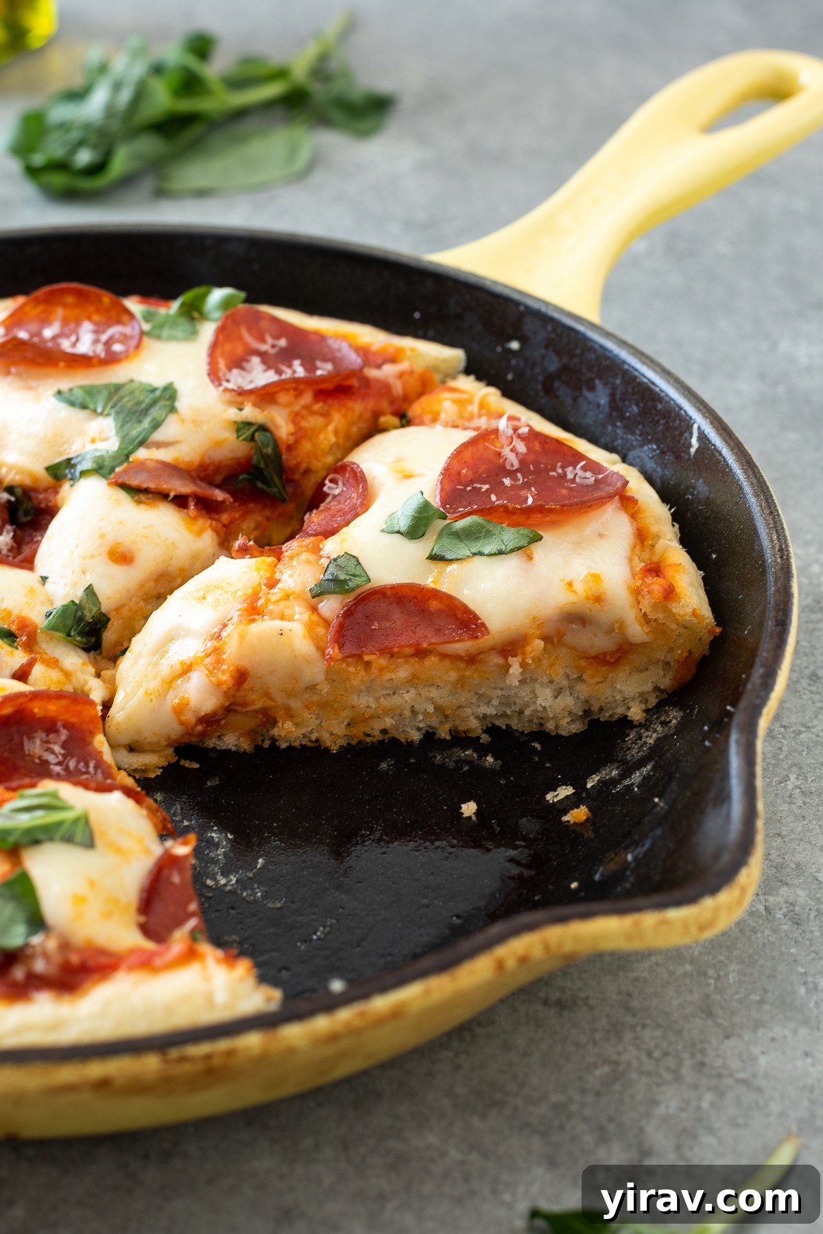 Easy focaccia pizza with pepperoni and basil, sliced in a cast iron skillet.