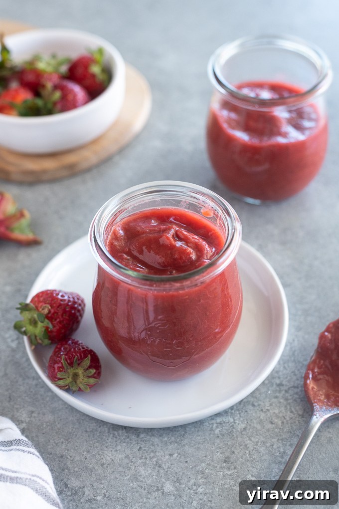 A jar of homemade rhubarb and strawberry jam with fresh strawberries arranged around it, emphasizing natural ingredients.