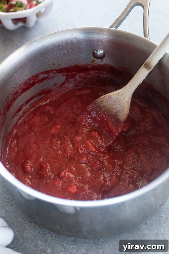 Homemade Strawberry Rhubarb Jam cooking in a saucepan, showing the fruit pieces breaking down and the liquid reducing to a thick consistency.