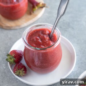 Homemade Strawberry Rhubarb Jam in a clear jar with a spoon, ready to be served.