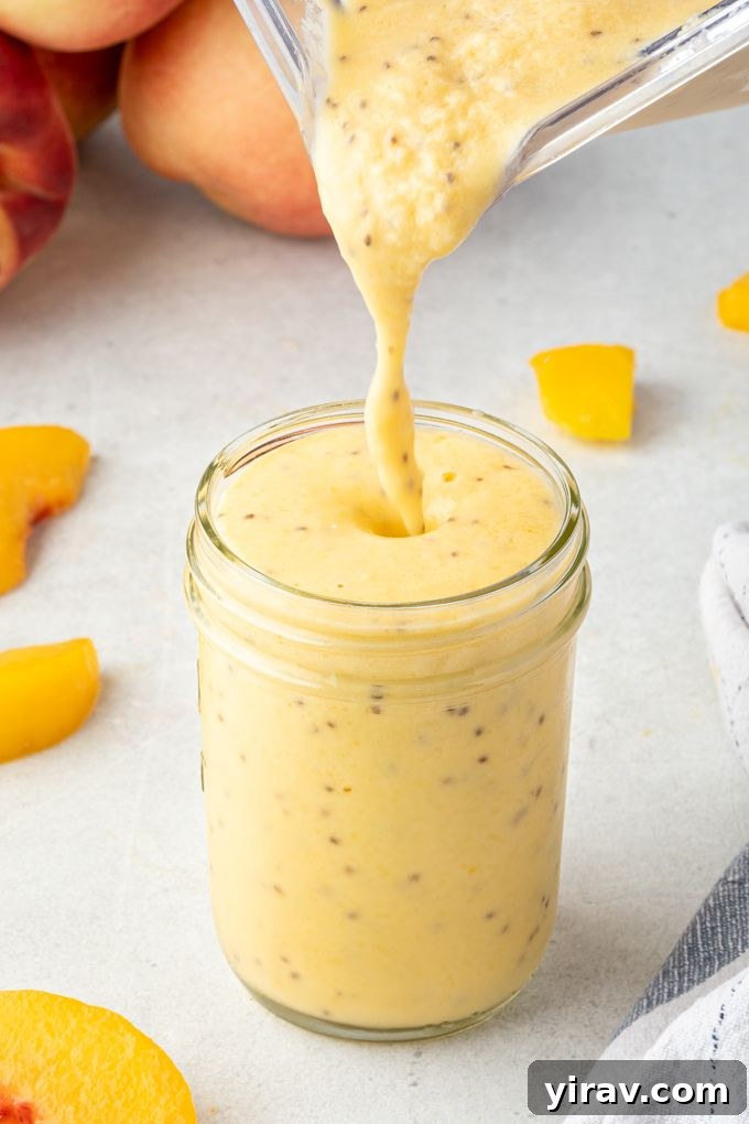 Sunshine Peach Mango Bliss 3 A stream of vibrant peach mango smoothie being poured from a blender into a tall glass jar, illustrating its smooth and inviting consistency.
