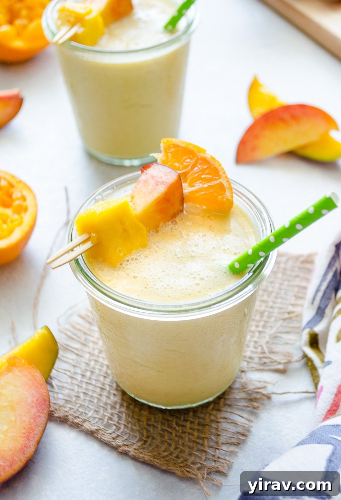 Sunshine Peach Mango Bliss 7 A refreshing peach mango smoothie in a modern glass jar with a reusable straw, garnished with a fresh peach slice and green leaf, on a light background.