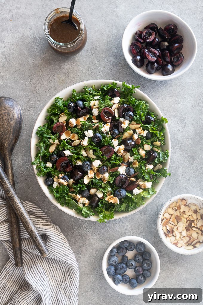 A large white bowl filled with summer kale salad, featuring vibrant cherries, blueberries, and goat cheese