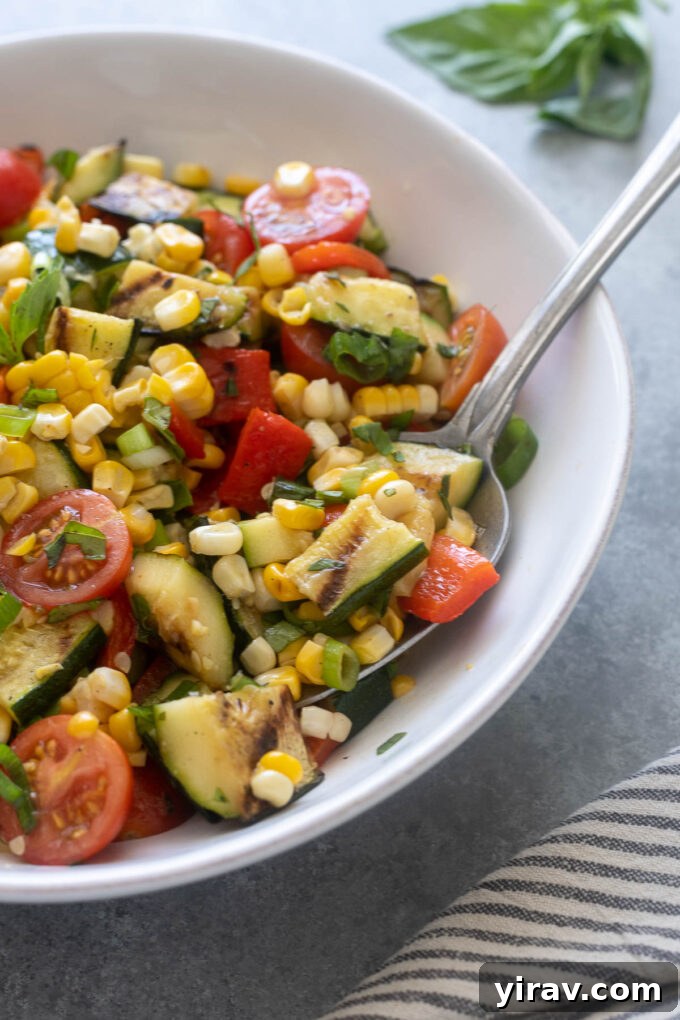 A serving spoon digging into a bowl of vibrant corn and zucchini salad.