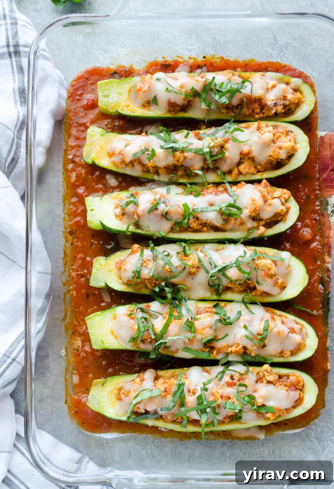 Close-up of golden brown Chicken Parmesan Stuffed Zucchini in a baking dish, showcasing melted cheese.
