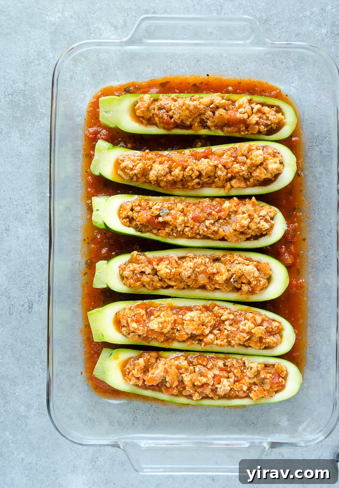 Stuffed zucchini with ground chicken parmesan filling, topped with cheese and ready for final baking.