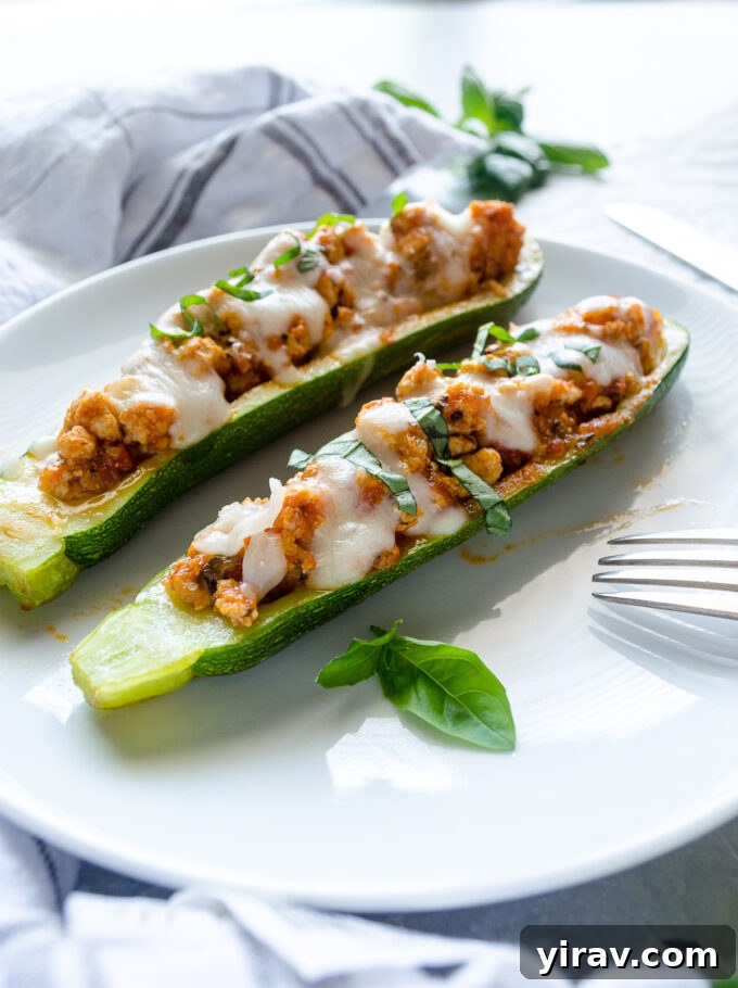 Two ground meat stuffed zucchini boats presented beautifully on a white plate, garnished with fresh basil.