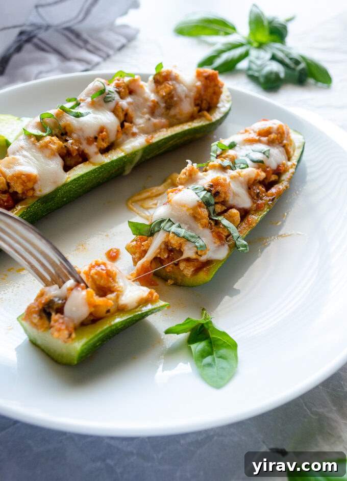 A close-up of Chicken Parmesan Stuffed Zucchini with a delightful cheese pull, emphasizing its gooey texture.