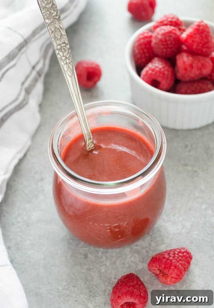 Vibrant Raspberry Vinaigrette 2 A jar of freshly made raspberry vinaigrette dressing with a spoon dipped inside, showcasing its vibrant color and luscious texture.