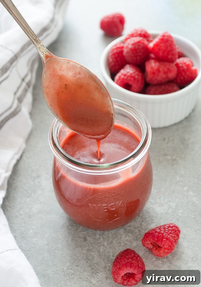 Vibrant Raspberry Vinaigrette 3 Fresh raspberry dressing drizzling from a spoon into a clear glass jar, highlighting its smooth consistency.