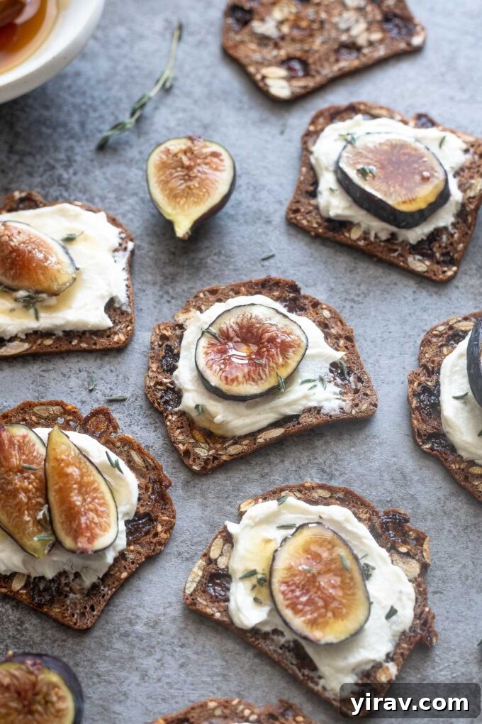 Whipped goat cheese with honey on crackers, adorned with fresh fig slices and a sprig of thyme, presented on a rustic wooden board.