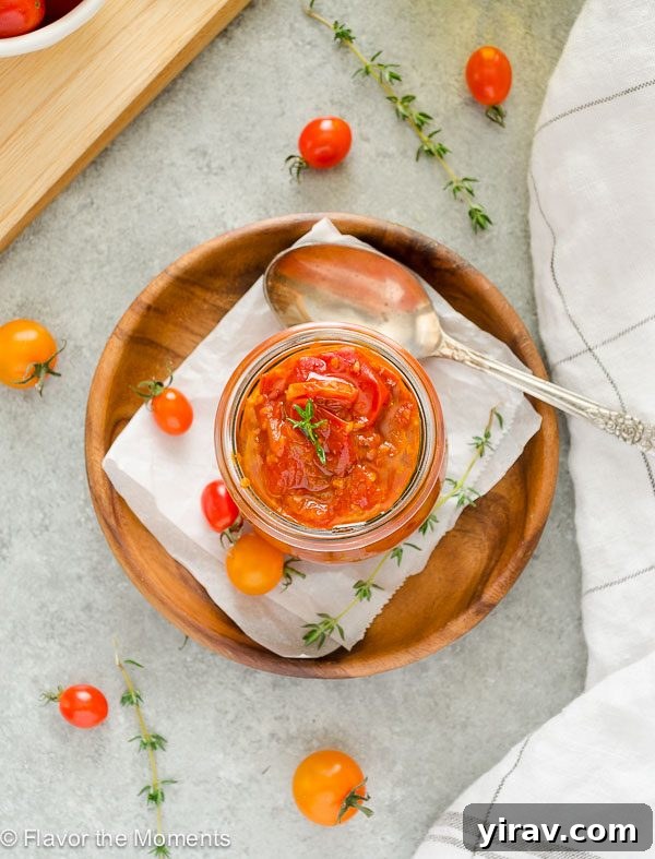 An inviting overhead shot of savory cherry tomato jam in a clear jar, resting on a stylish teak plate, garnished with fresh thyme.