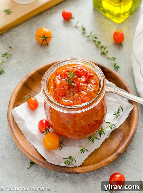 Close-up of small batch cherry tomato jam in a jar, with a spoon resting in it, highlighting its rich texture and inviting color.