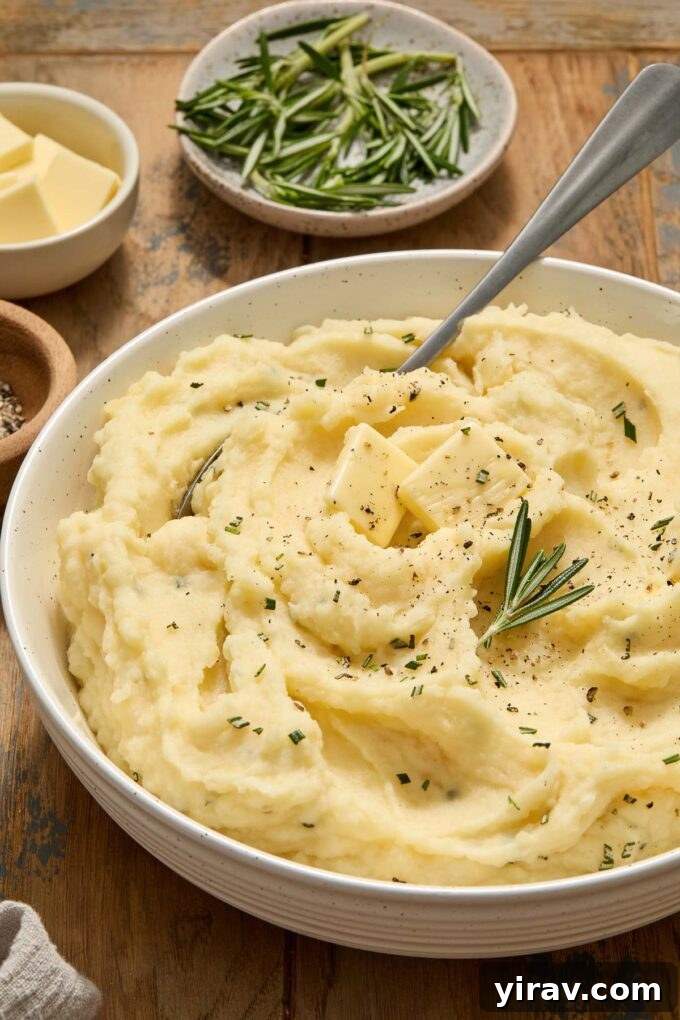 Buttermilk mashed potatoes in a white bowl, ready to be served, garnished with fresh herbs.