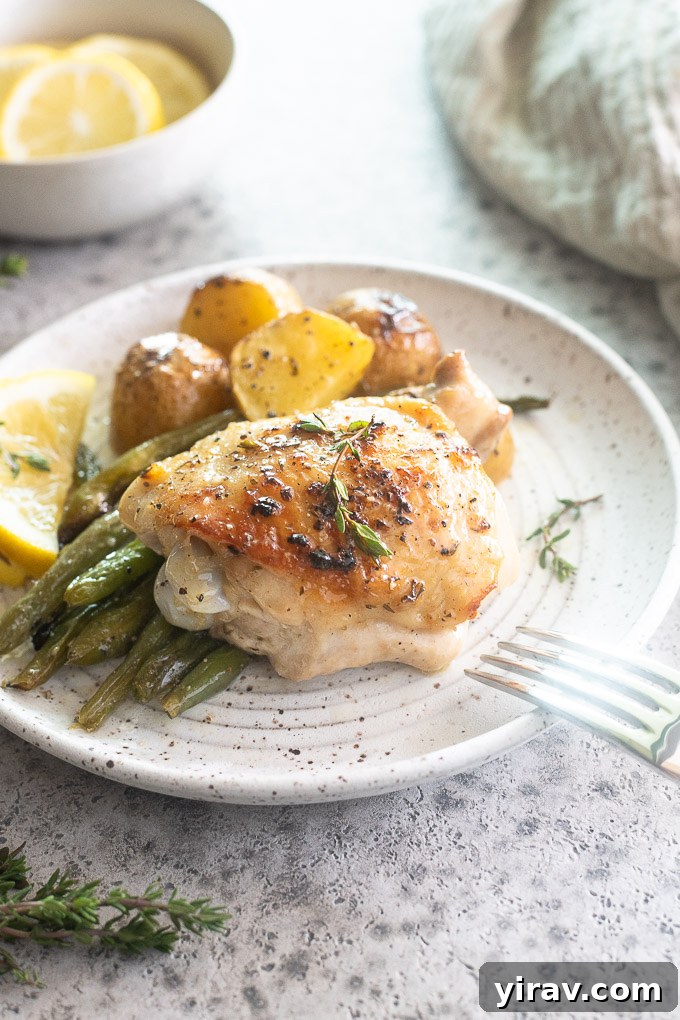 Sheet pan chicken thighs on a plate with potatoes and green beans.