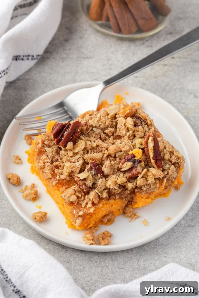 Serving of sweet potato casserole with streusel topping on a plate, garnished with fresh herbs