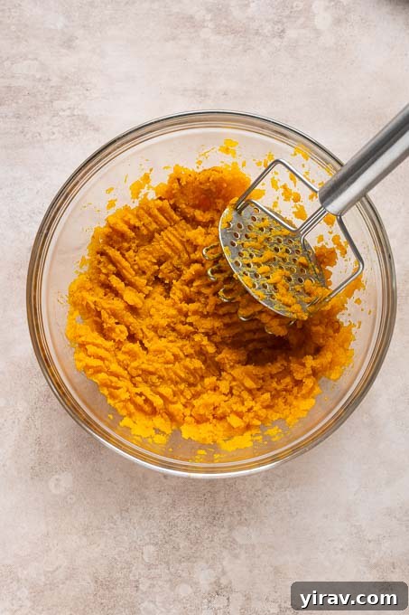 Velvet Kabocha Puree 9 Mashed kabocha squash in a large bowl with a potato masher.