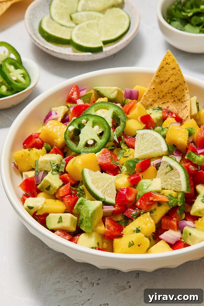 Close-up of Mango and Avocado Salsa in a decorative bowl, garnished with fresh lime slices and a jalapeño pepper.