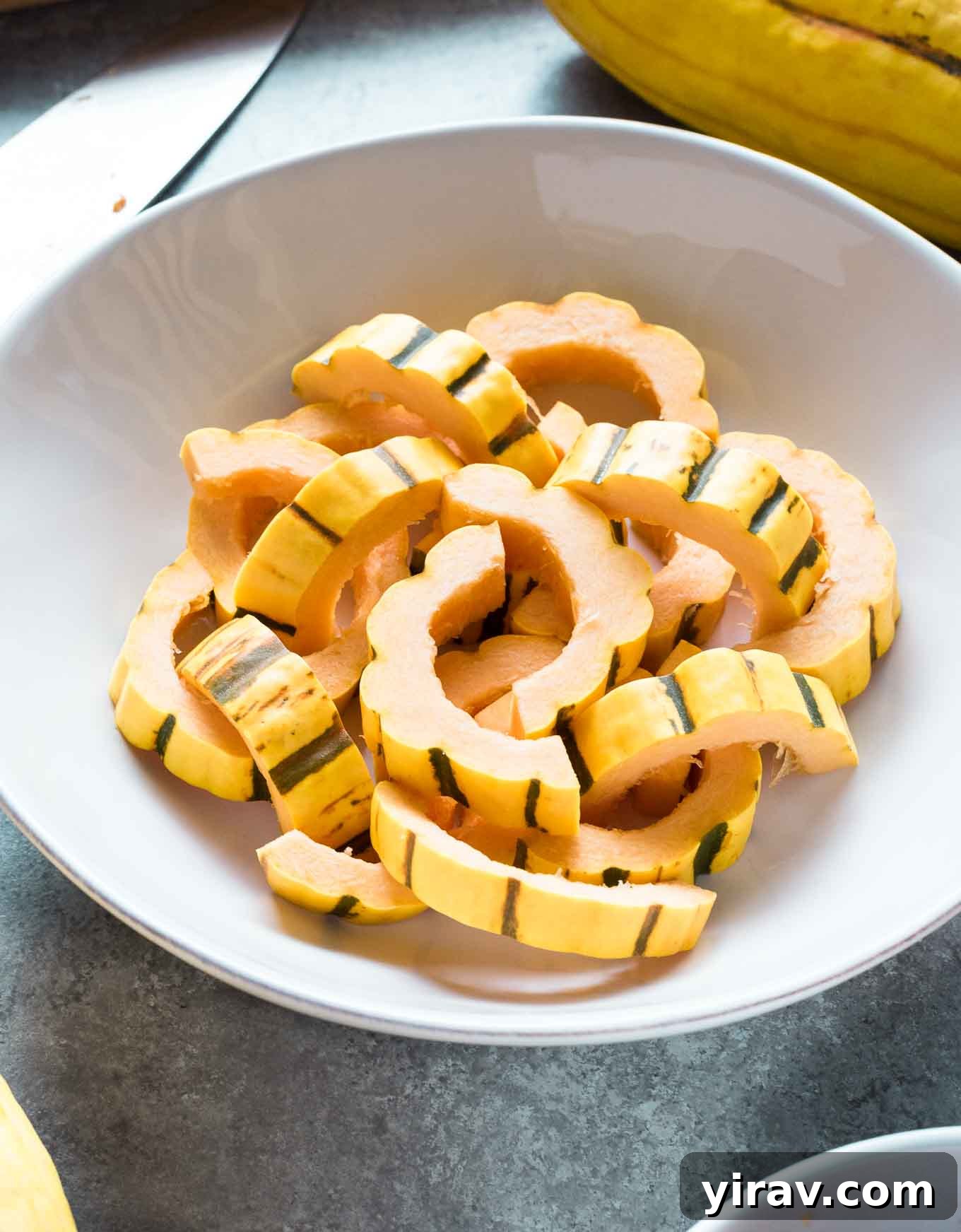A pristine white bowl filled with neatly prepared and sliced delicata squash, ready for the next step in a delicious recipe.