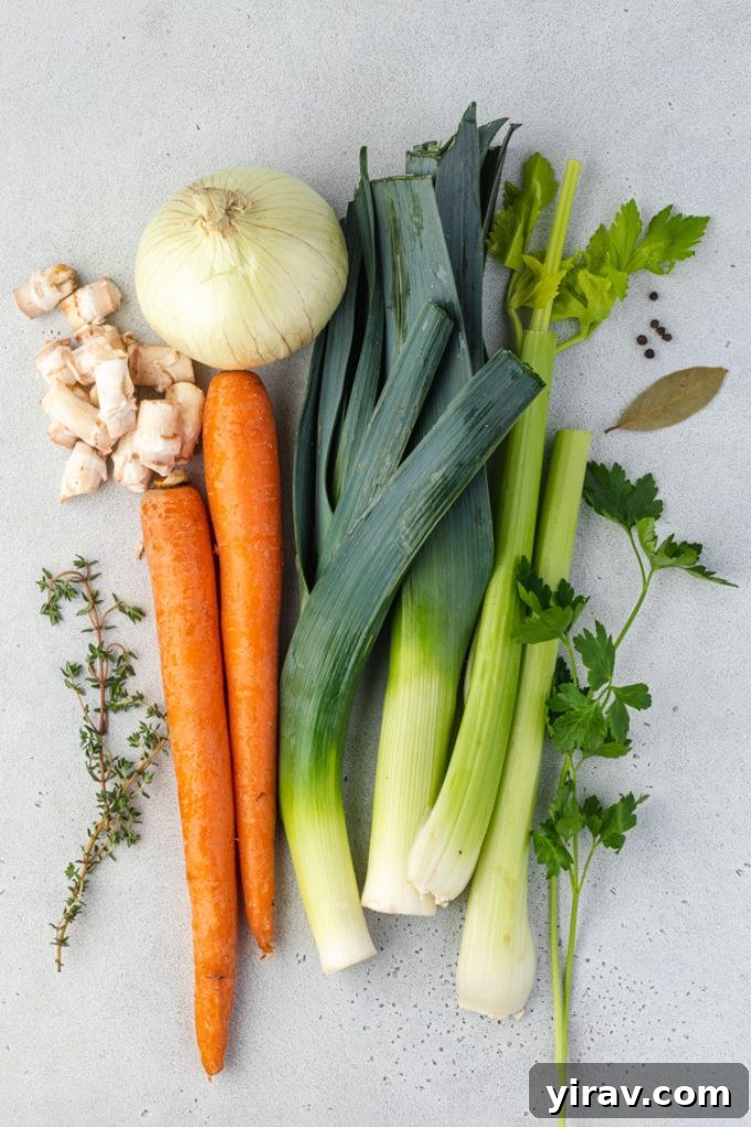 A collection of fresh ingredients laid out, including whole onions, carrots, celery stalks, mushroom caps, bay leaves, thyme sprigs, and peppercorns, ready for making vegetable stock.