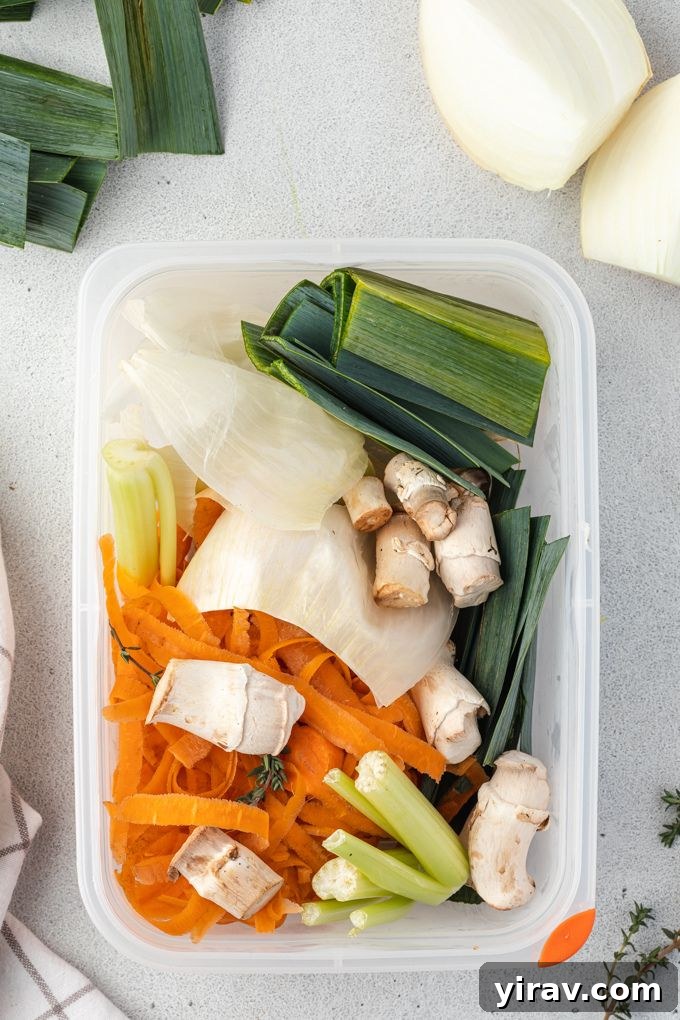 A transparent Stasher bag filled with assorted vegetable scraps like onion peels, carrot ends, and mushroom stems, ready to be used for homemade stock.